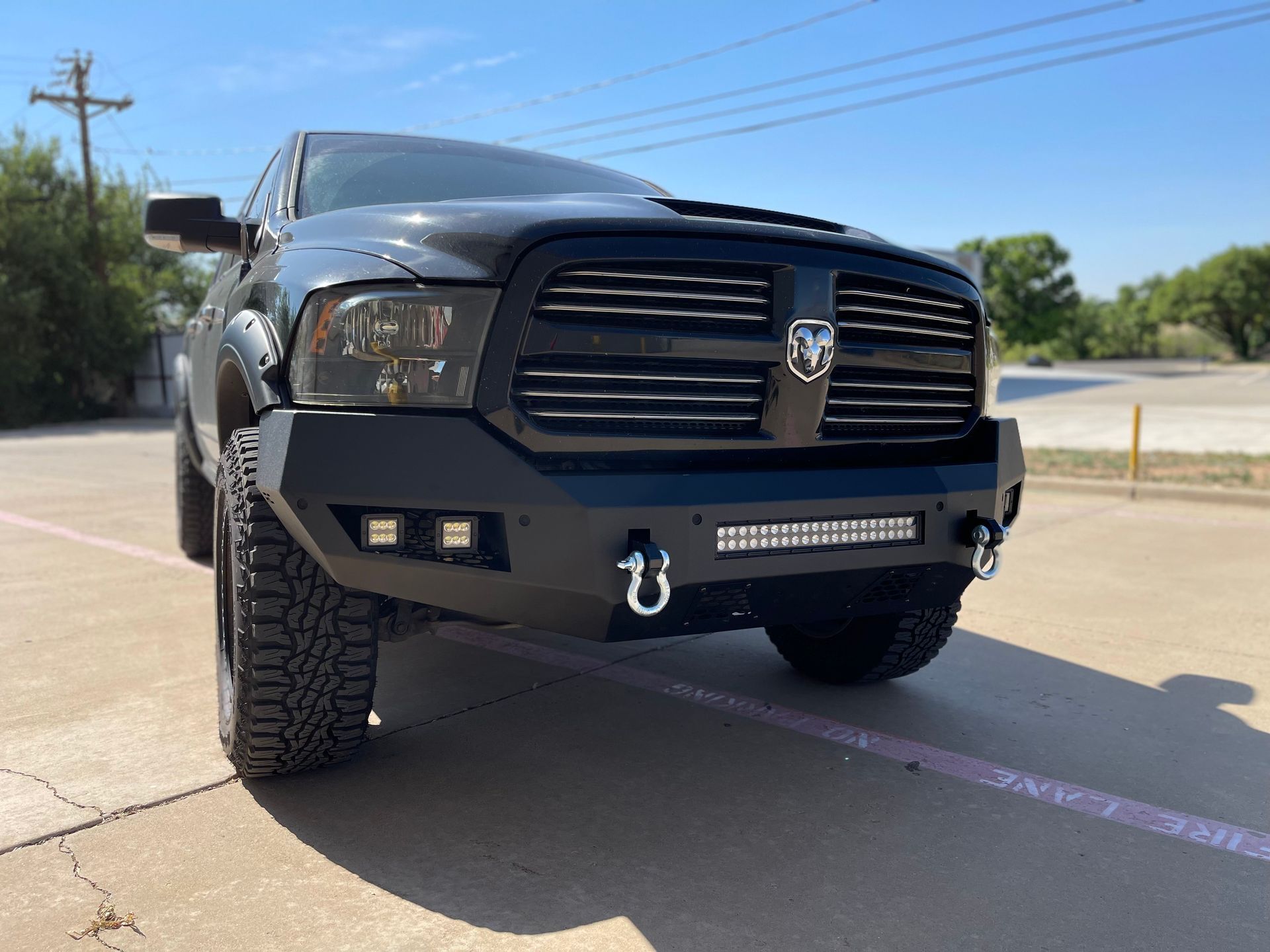 Black Ram truck with modified front bumper and off-road tires, parked outdoors on a sunny day.