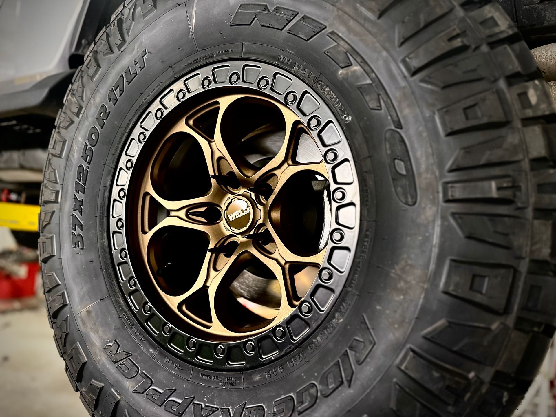 Close-up of a bronze and black custom off-road wheel and tire mounted on a vehicle.