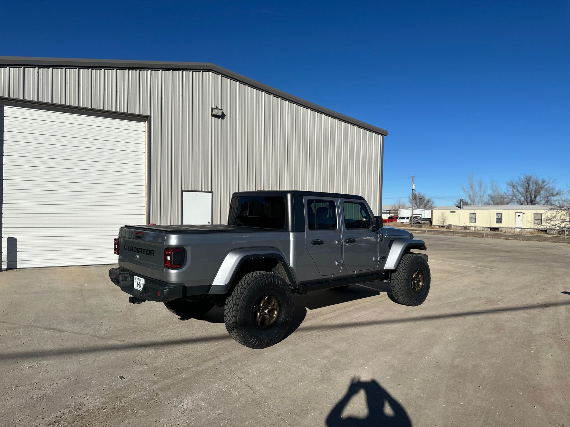 Gray Jeep Gladiator truck parked near a warehouse on a sunny day.