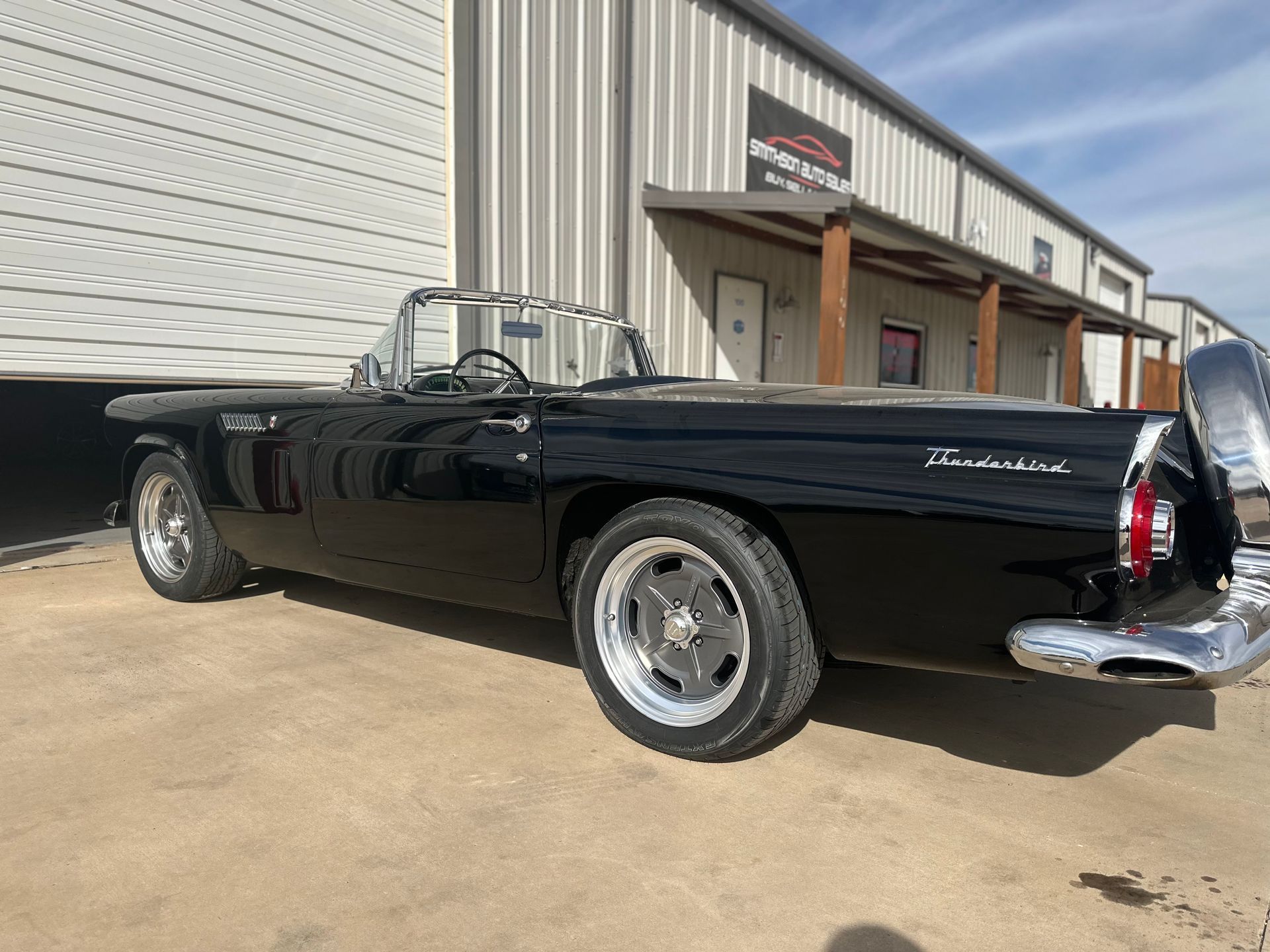 Black vintage Ford Thunderbird convertible parked outside a building.