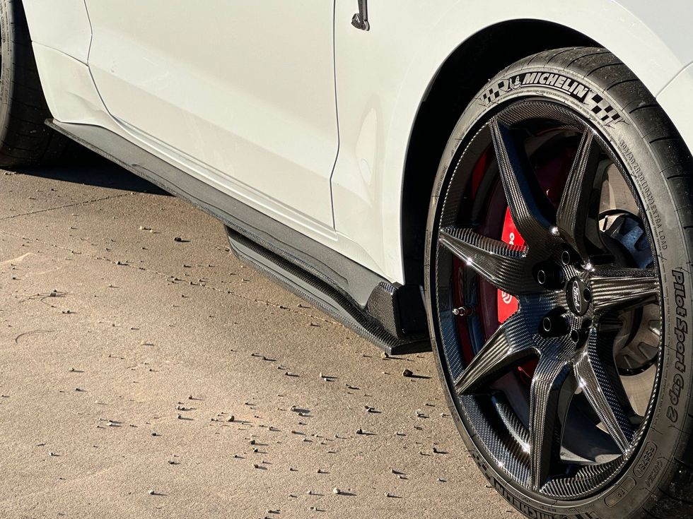 White car with black side skirt and carbon fiber wheels, red brake calipers.