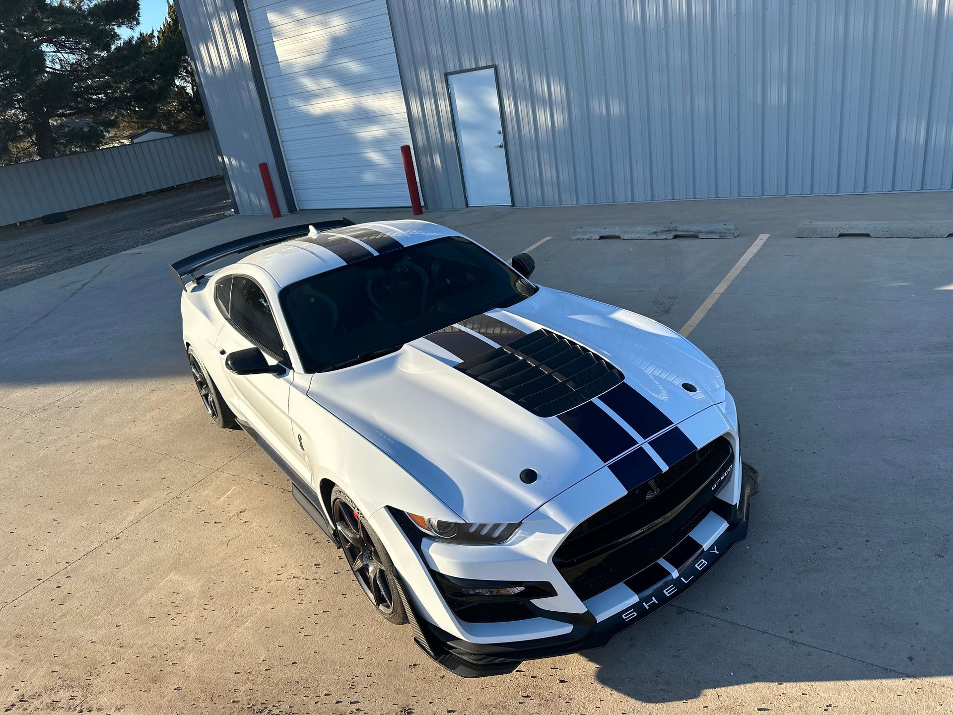 White Ford Shelby Mustang with black stripes parked outside a building.
