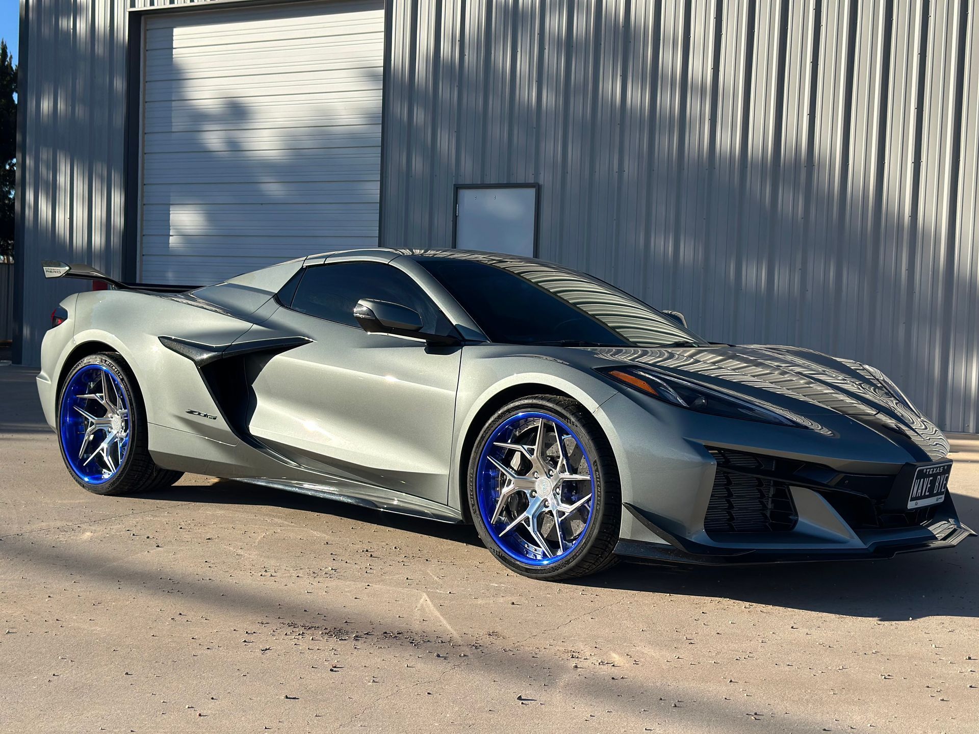 Gray Chevrolet Corvette with blue rims parked outside a building.