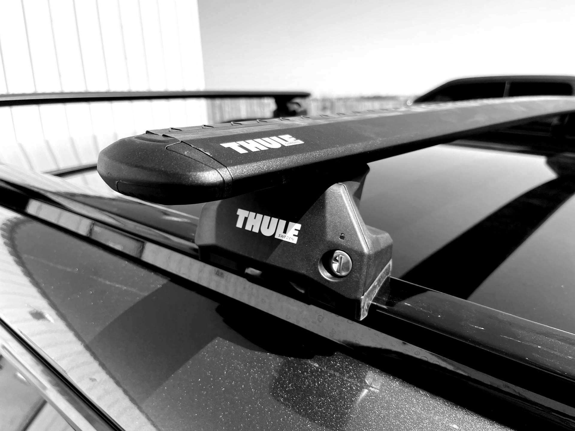 Black and white close-up of a Thule roof rack mounted on a car.
