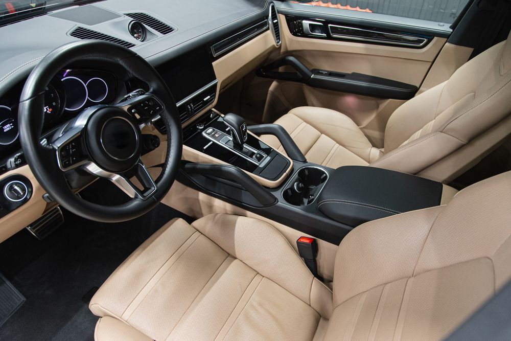 Interior of a tan-leather Porsche SUV with a black dashboard and steering wheel.
