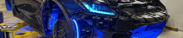 Front end of a black car with blue lights. The car is partially lifted. The lights are blue.