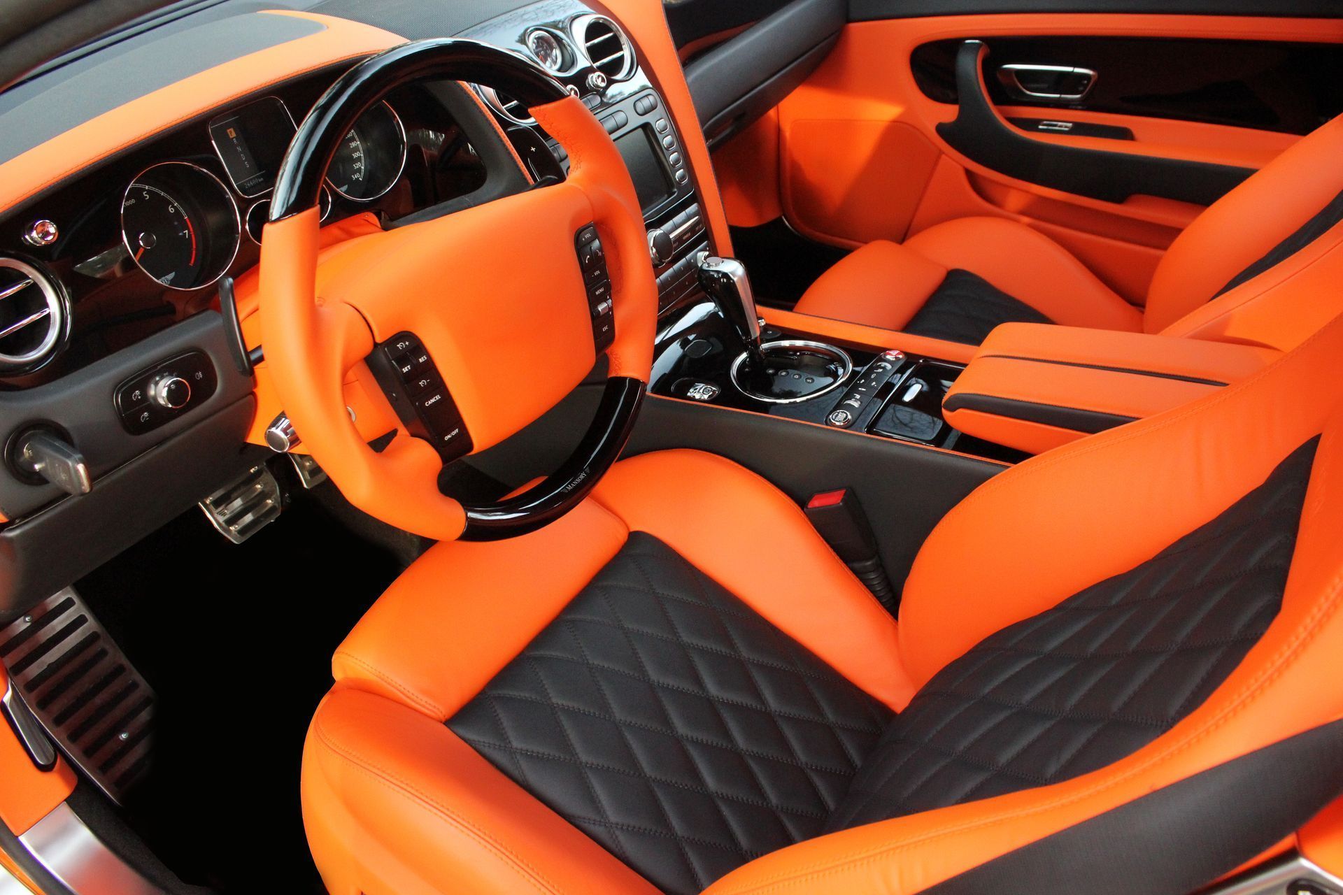 Bright orange and black Bentley interior with leather seats, steering wheel, and dashboard.