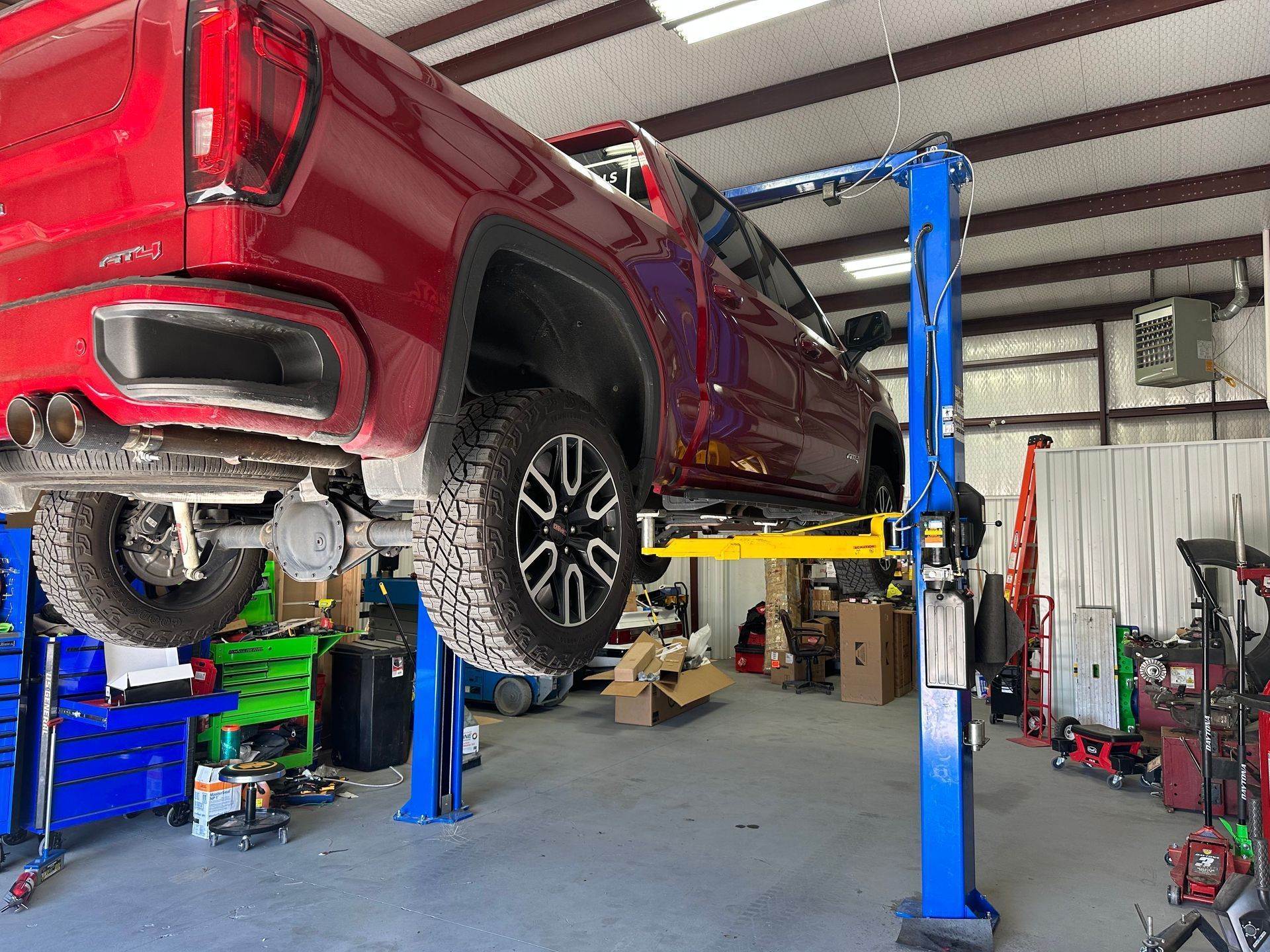 Red pickup truck on a blue automotive lift in a workshop.