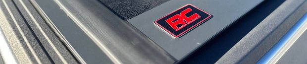 Red and black RC logo on a gray surface with parallel grooves.