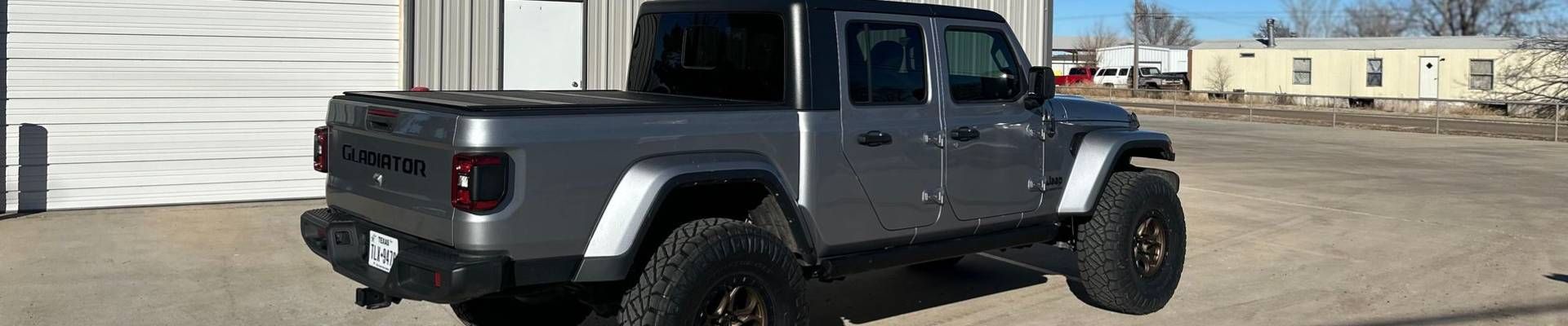 Gray Jeep Gladiator truck parked outside a building on a sunny day.