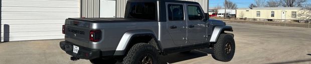 Gray Jeep Gladiator truck parked outside a building on a sunny day.