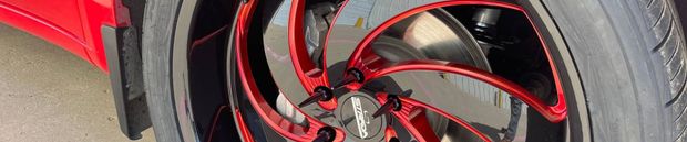 Close-up of a red rim on a tire. The rim has a shiny, metallic finish and a pattern of red spokes.