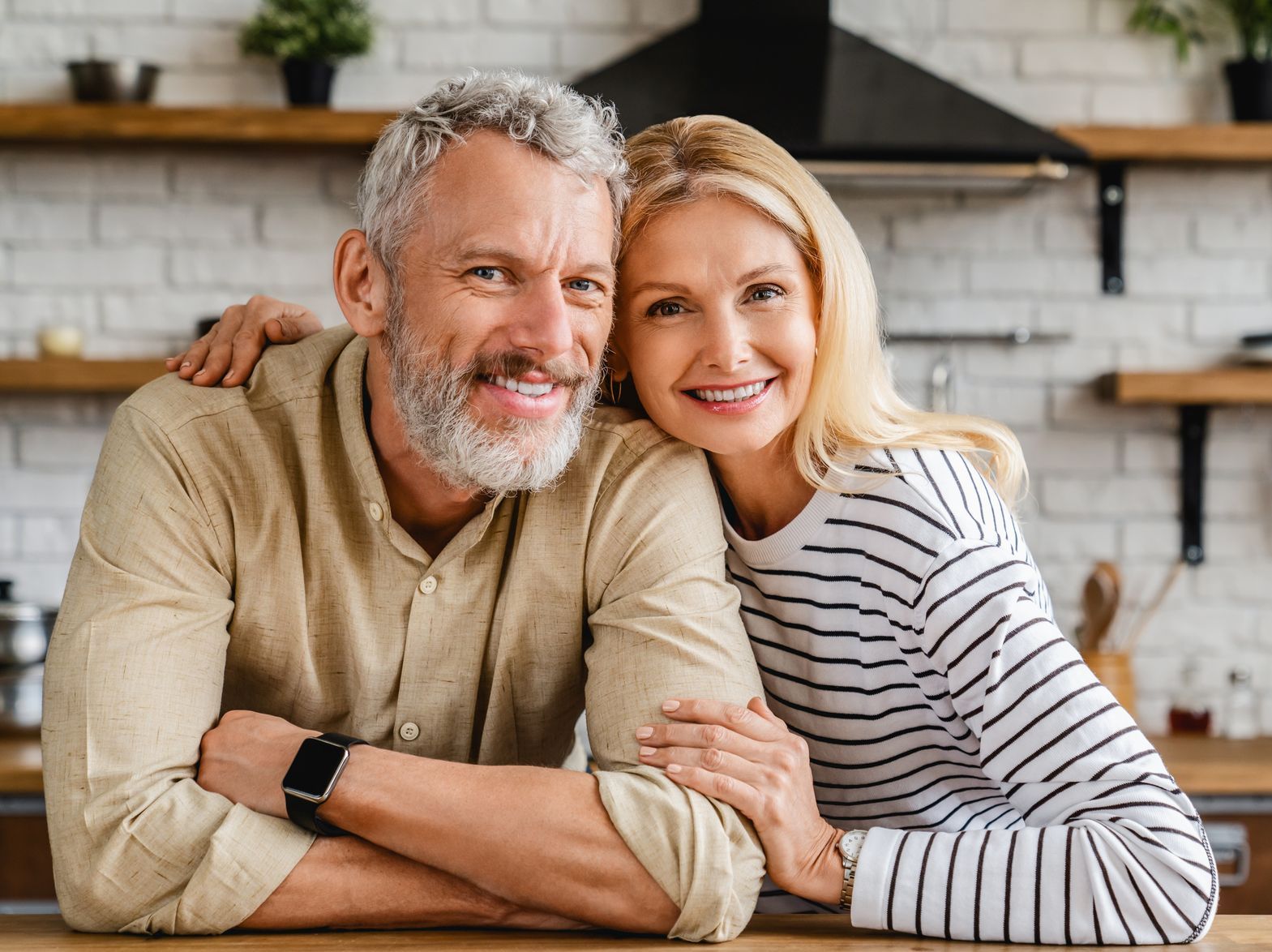 A man and a woman are posing for a picture in a kitchen.