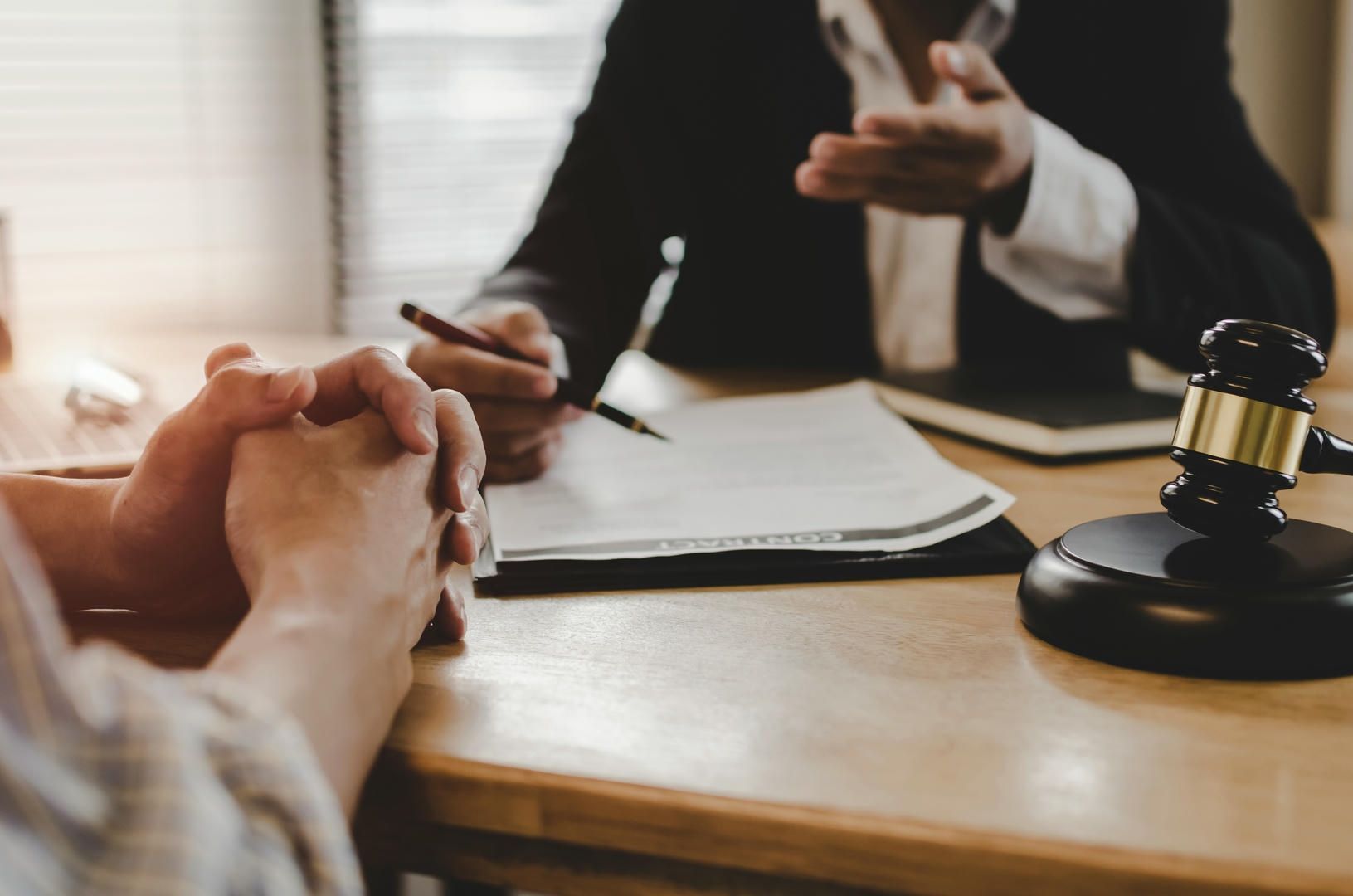 Lawyer and client in a meeting, gavel on desk, paperwork, hands clasped.