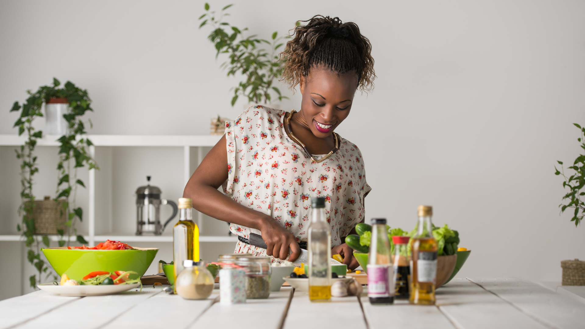 Person preparing food in a bright kitchen, arranging ingredients on a table with plants and cookware nearby