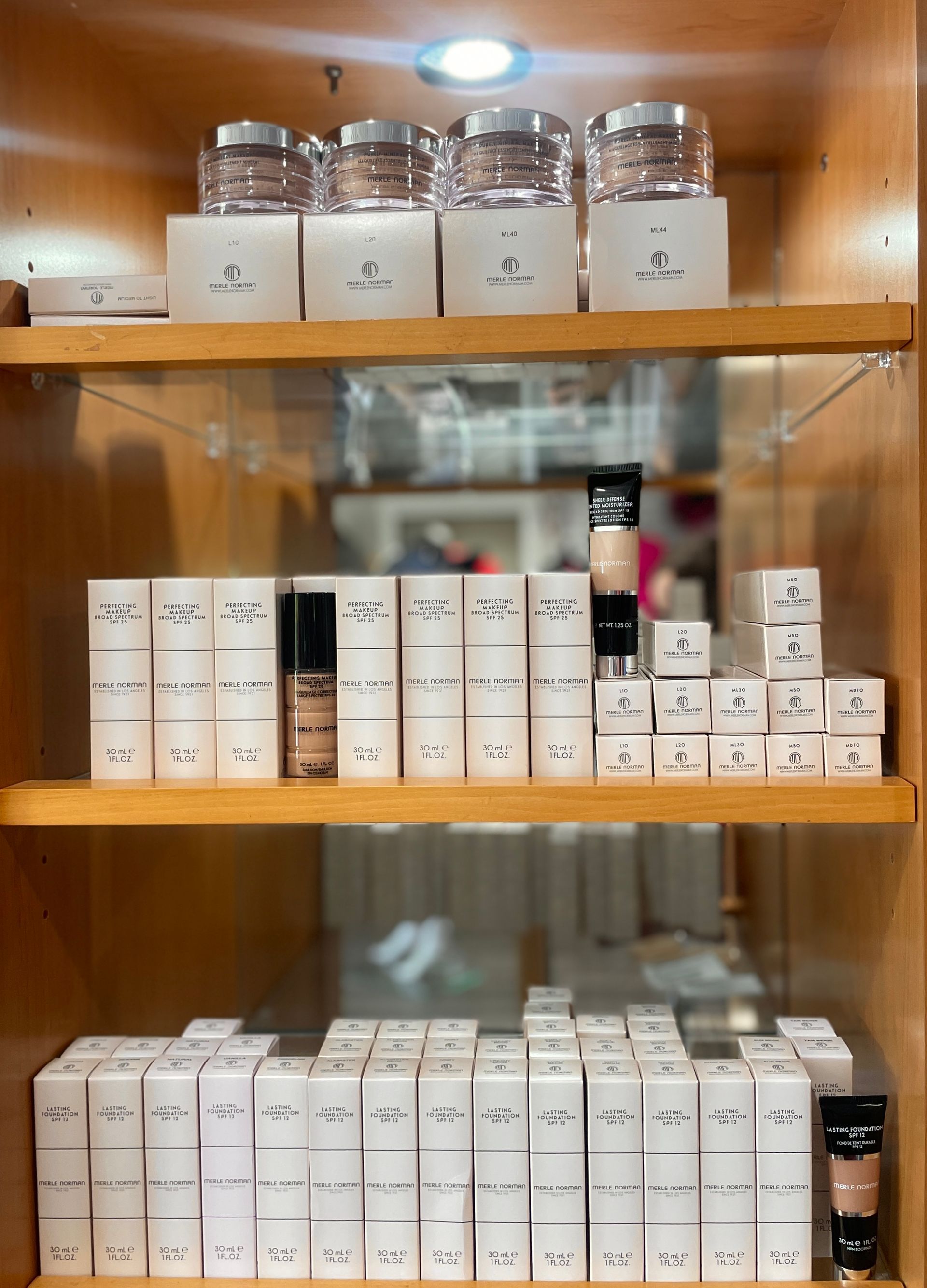 A makeup artist in a black blazer applies foundation with a brush to a client wearing a white robe in a studio.