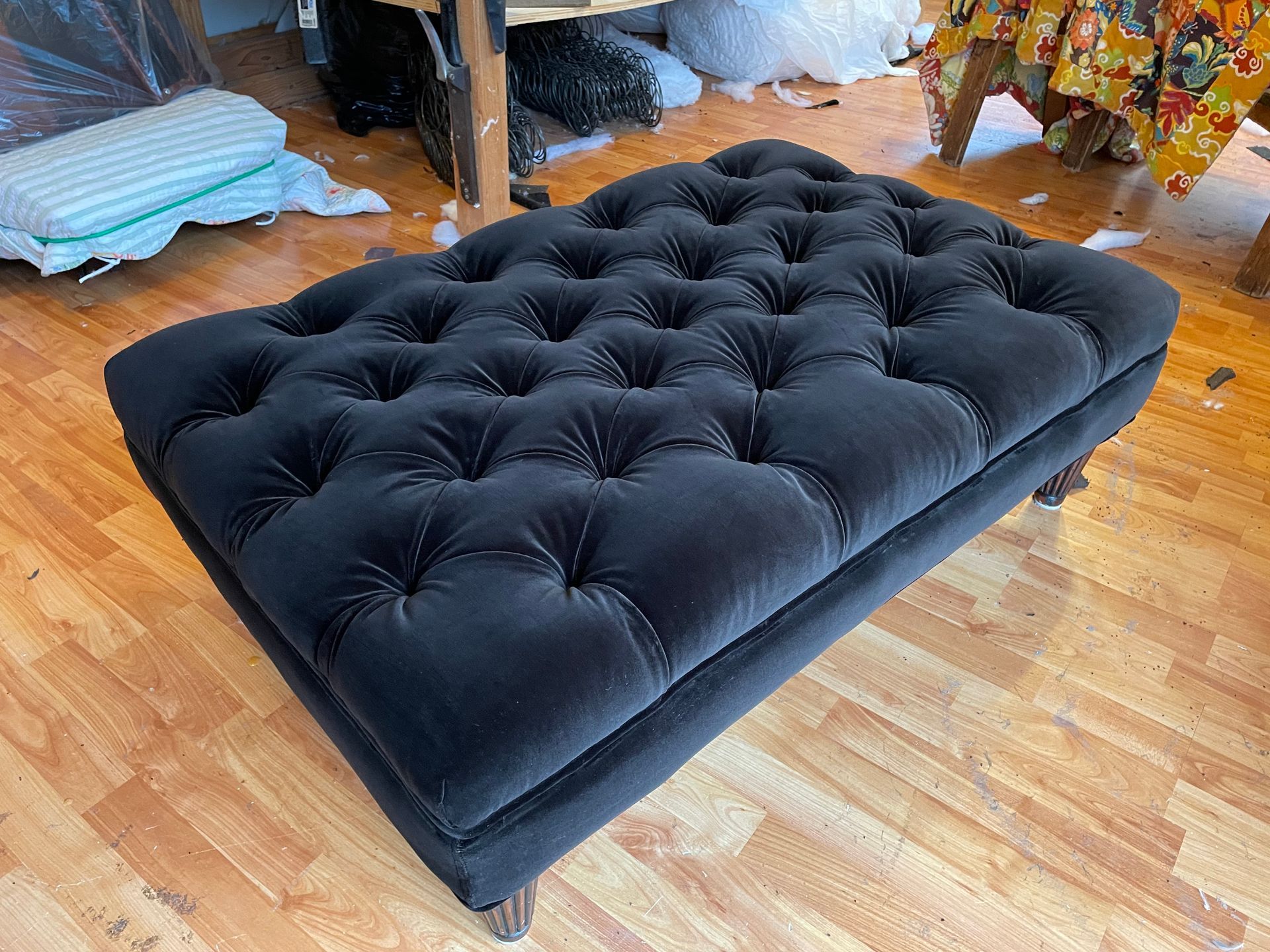 A black tufted ottoman is sitting on a wooden floor.