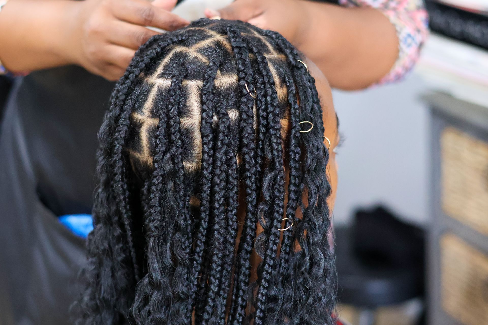 Braids being styled on a person's head; hands working on the hair.