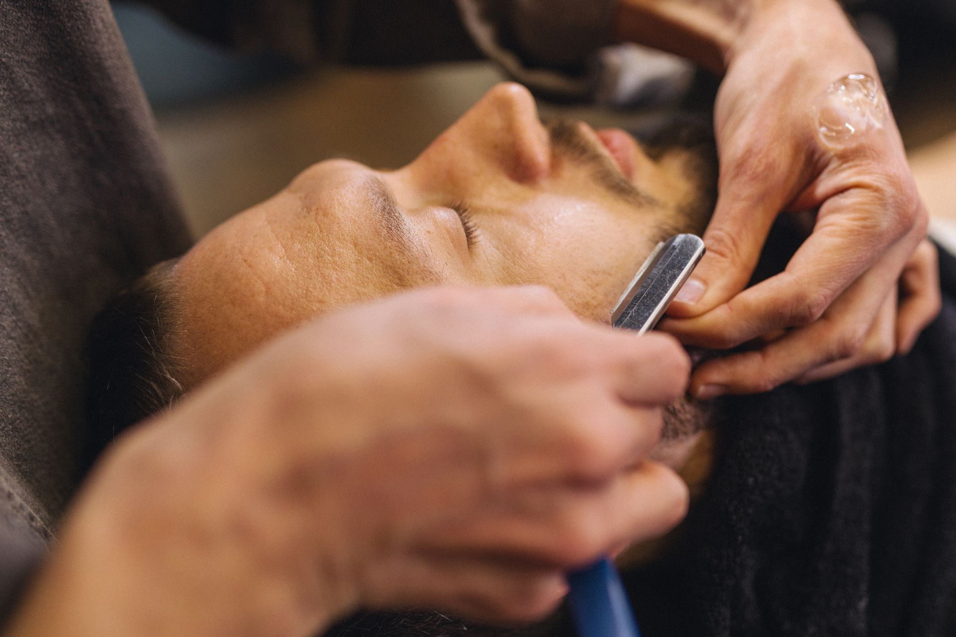 Barber shaving a person's beard with a straight razor.