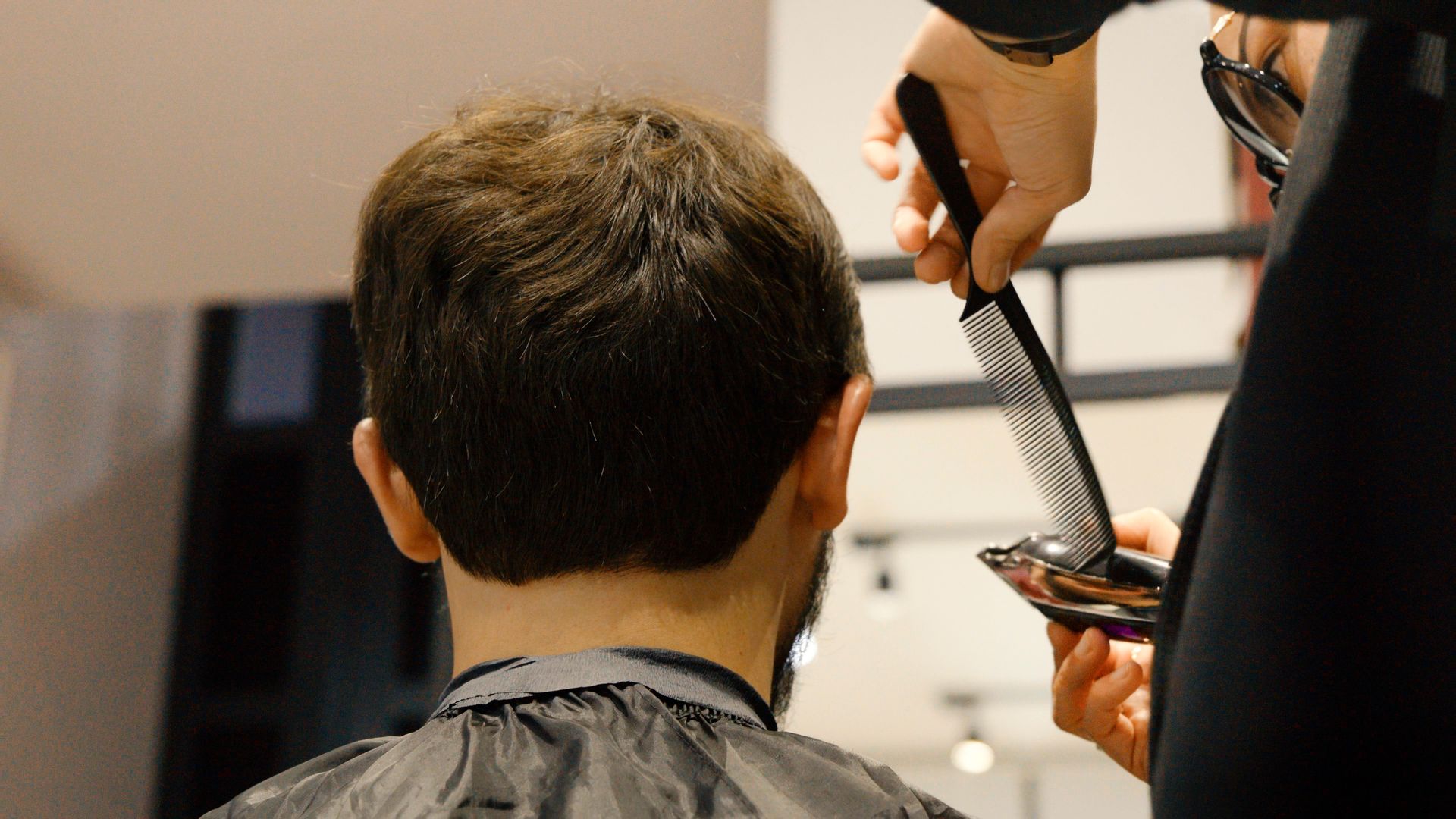 Barber cutting client's hair with comb and scissors in a salon.