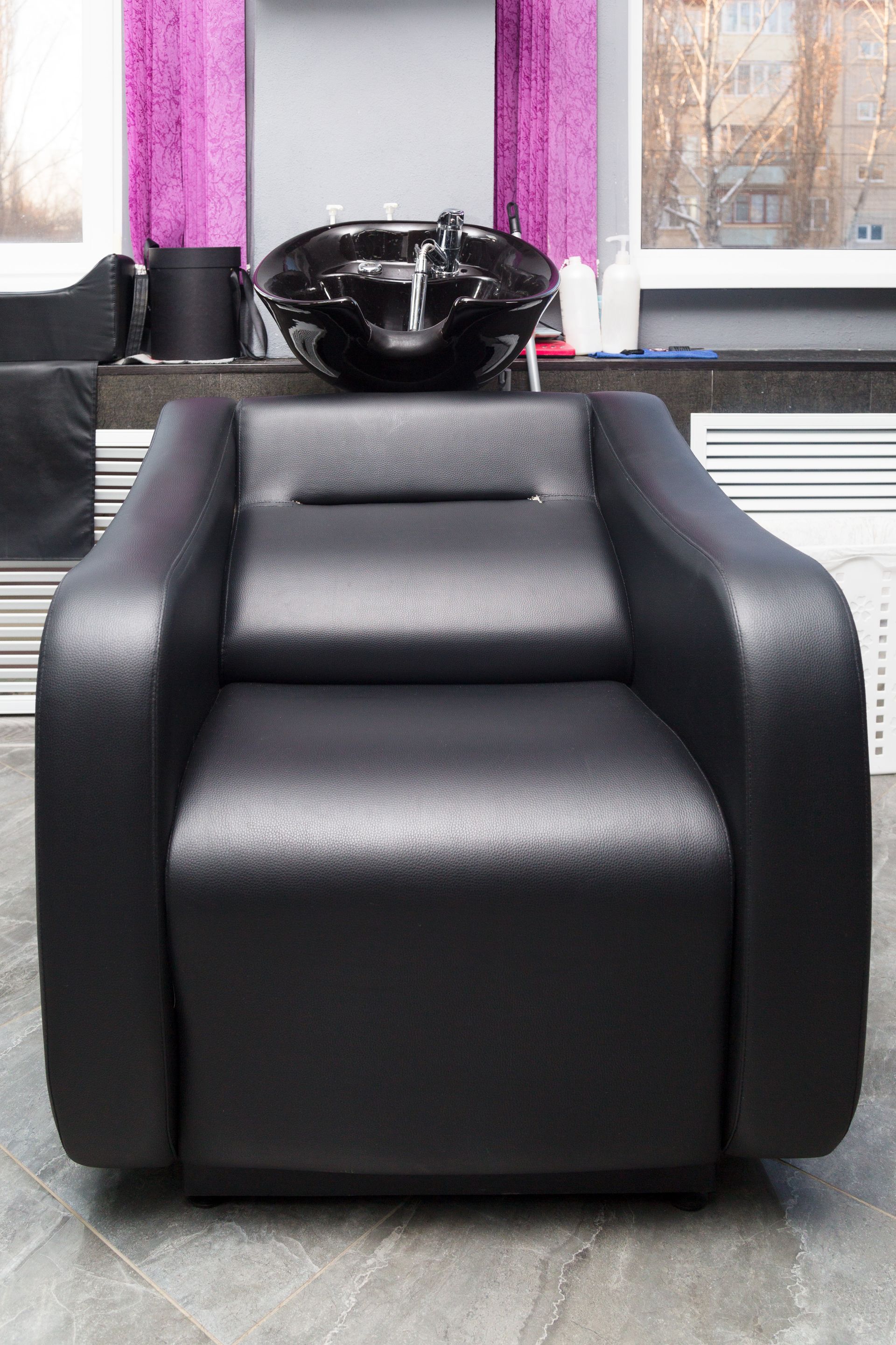 Black hair salon chair with sink, purple curtains in the background.
