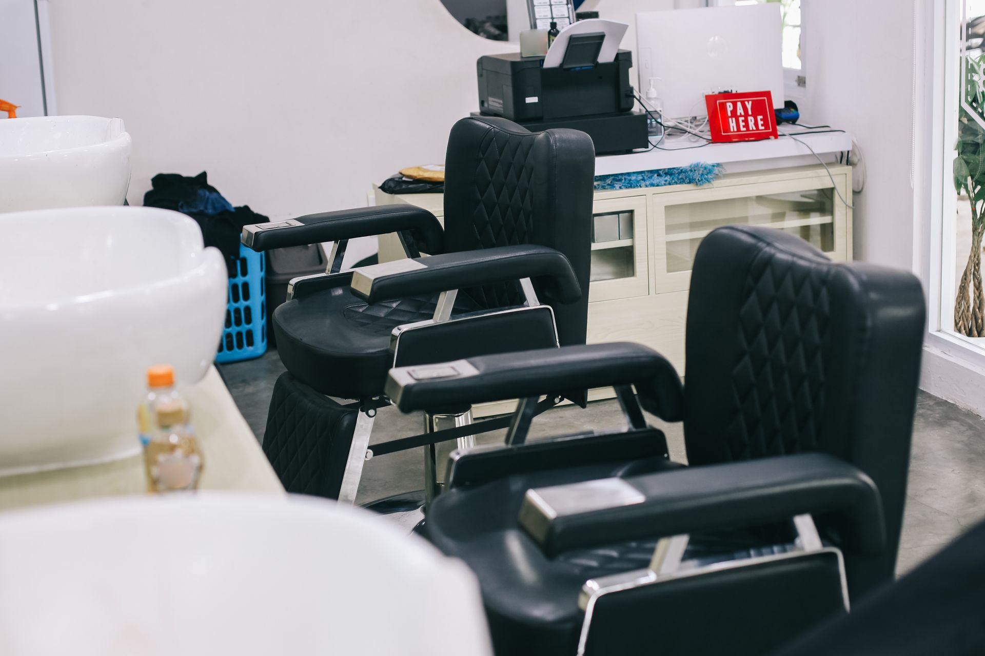 Barber shop interior with black chairs, white sinks, and equipment on a counter.