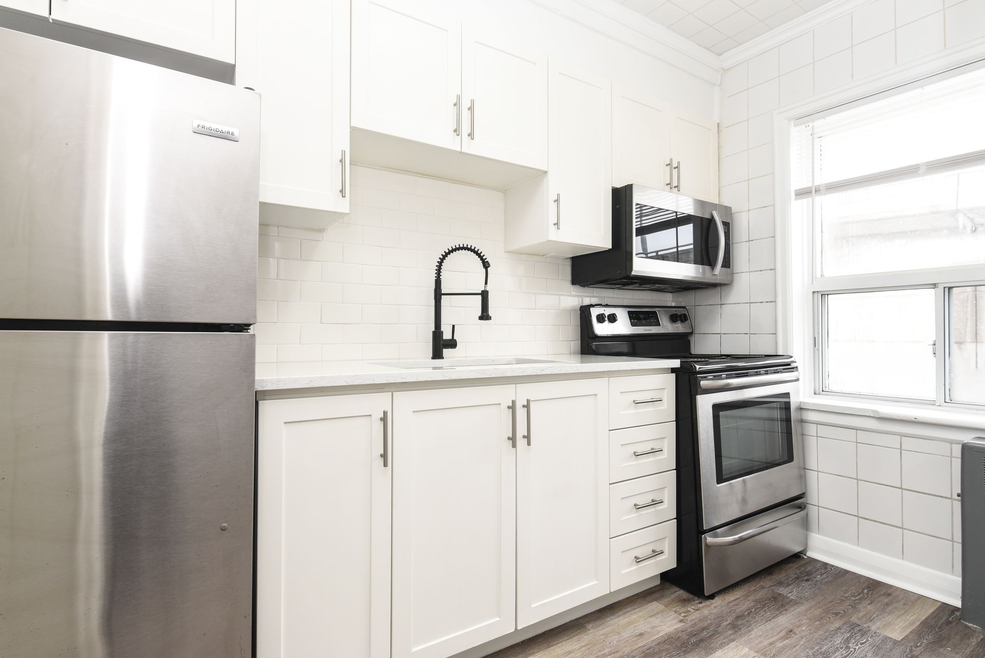 Bright white modern kitchen with stainless steel appliances, black faucet, and large window.