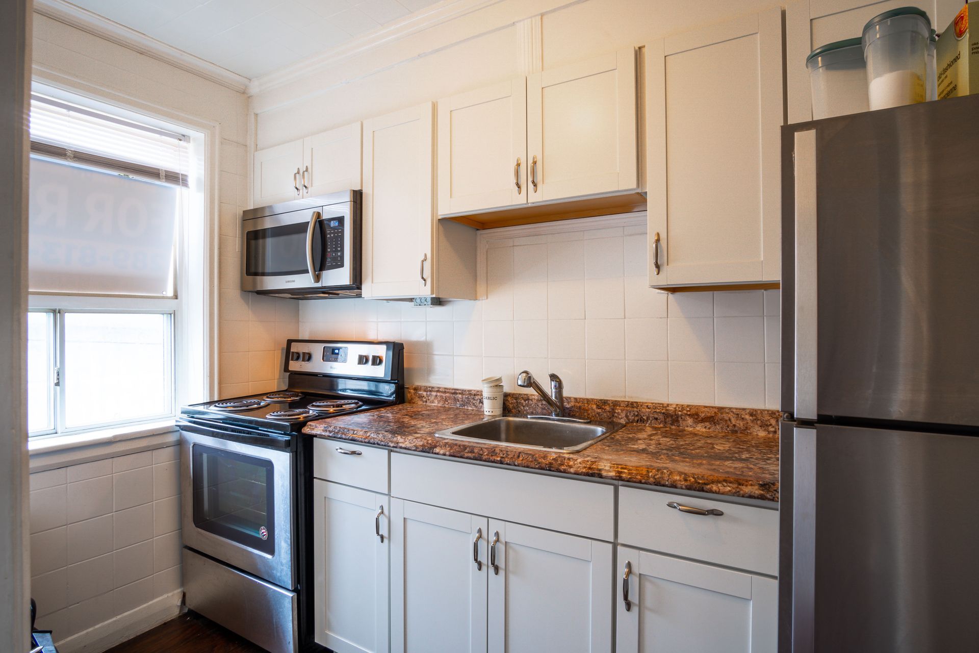 Bright white kitchen with stainless steel appliances, granite countertops, and a window by the sink.