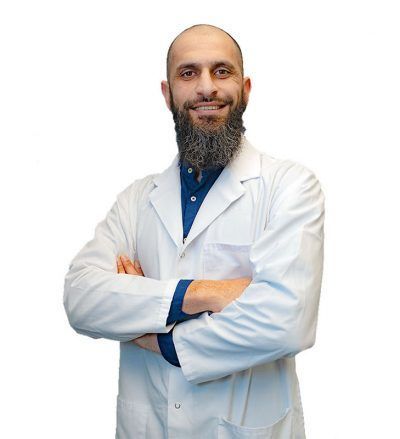A man with a beard is wearing a white lab coat and smiling with his arms crossed.