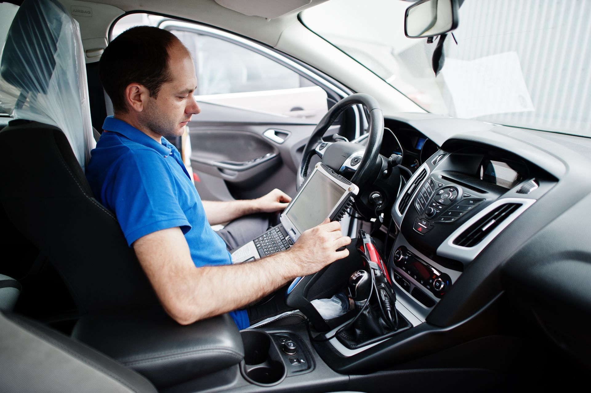 A man is sitting in the driver 's seat of a car using a laptop.