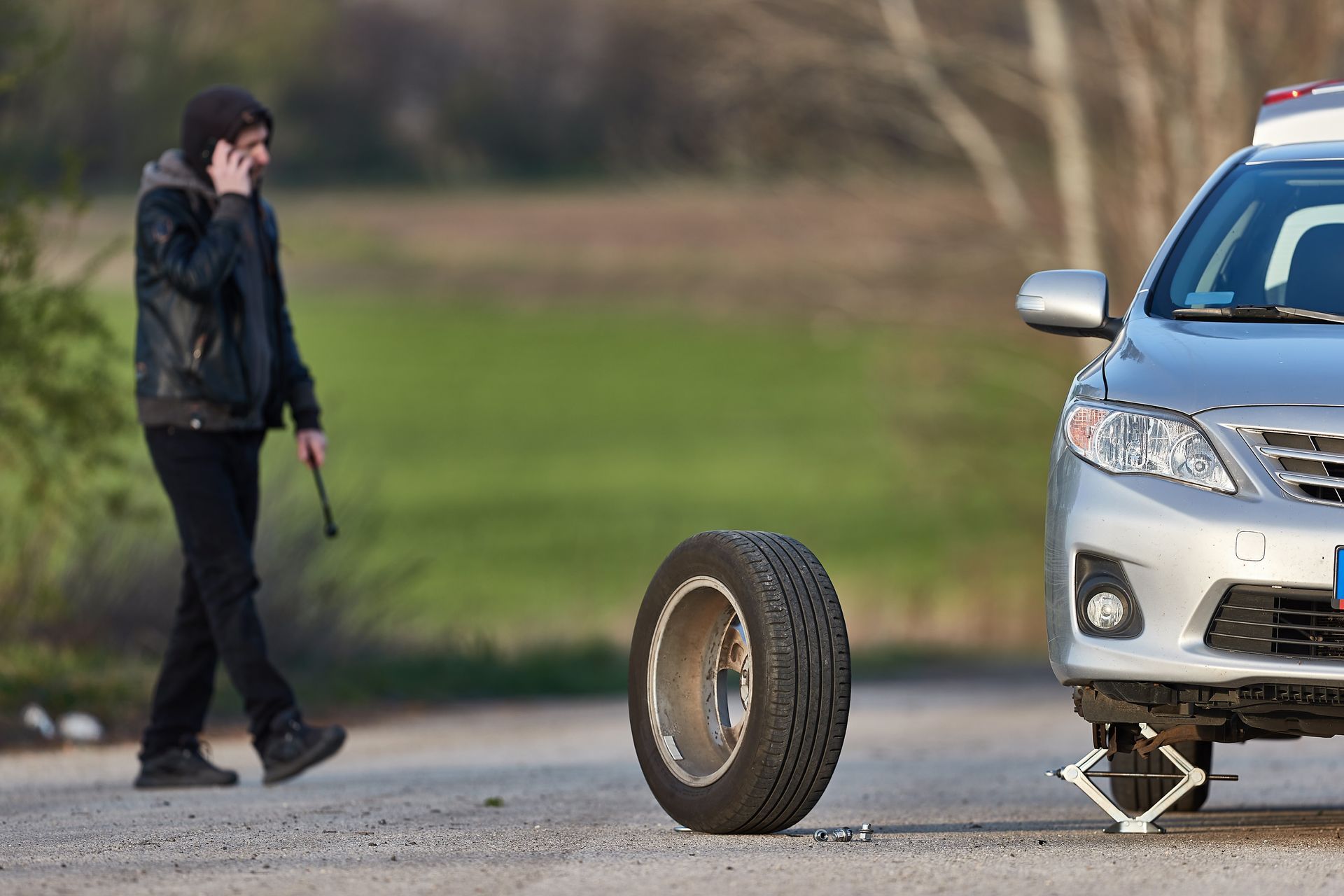 A man is talking on a cell phone next to a car with a flat tire.
