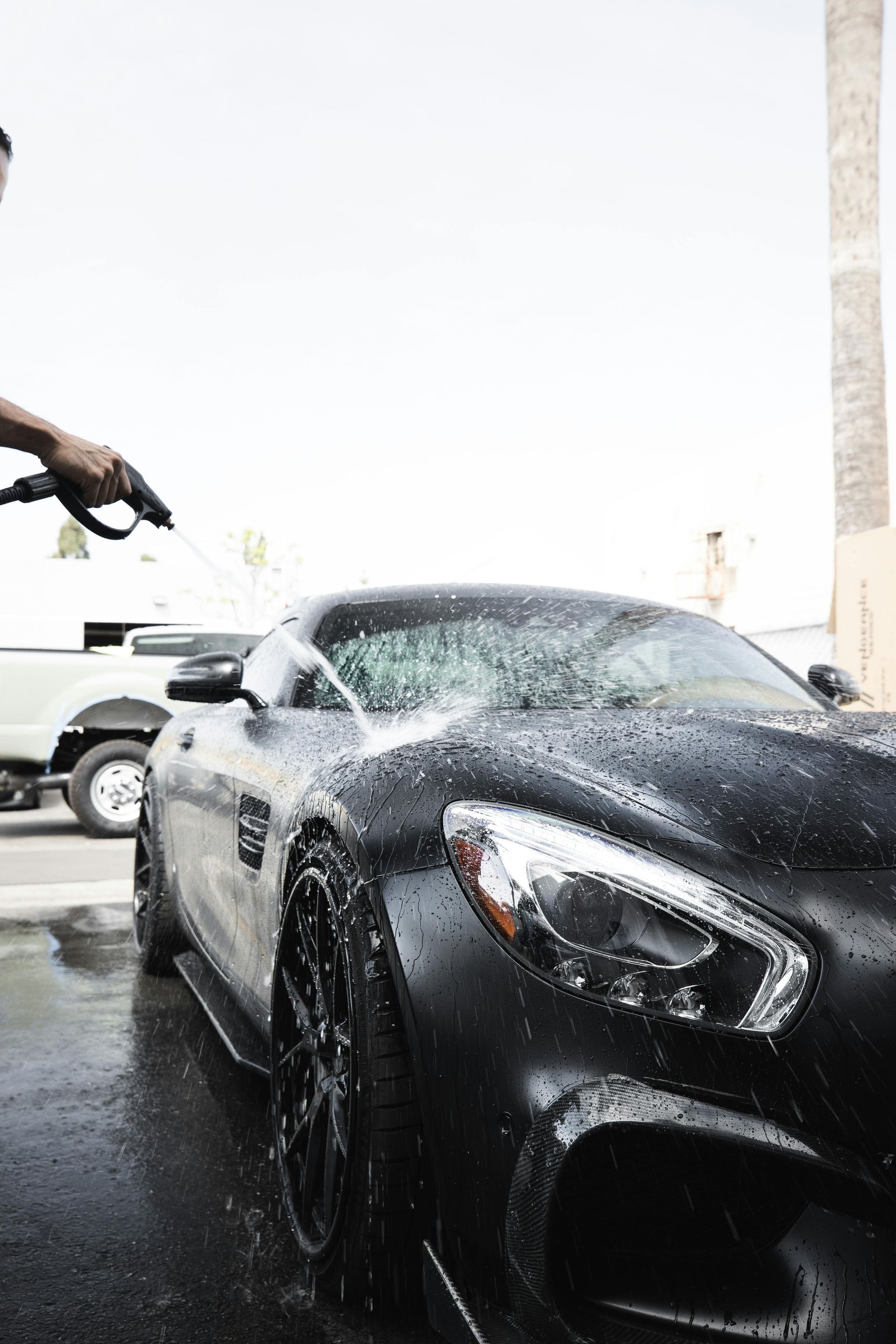 Black sports car being sprayed with water at a car wash, with foam on the hood and windshield.