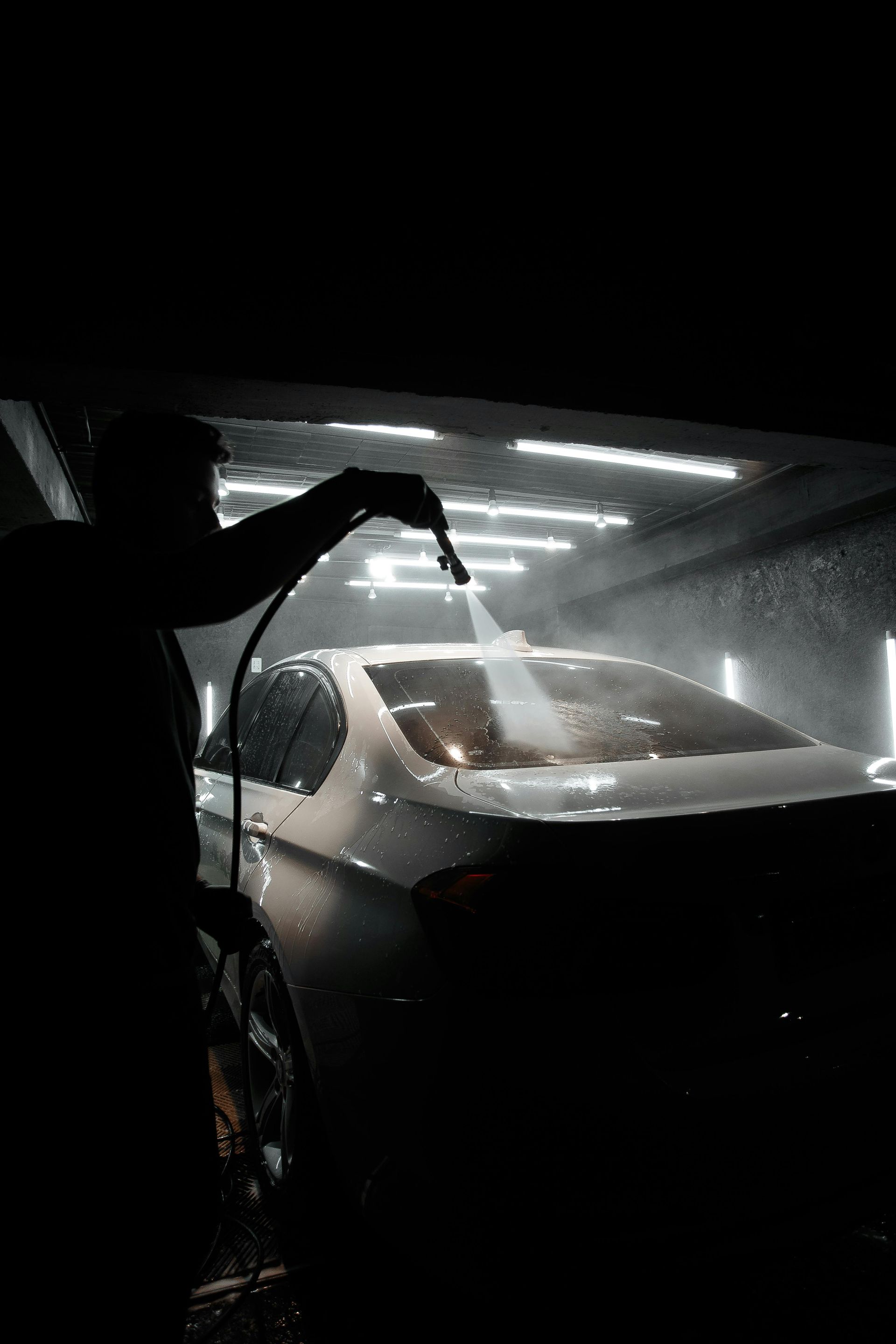 Person washing a white car in a dark garage under bright overhead lights