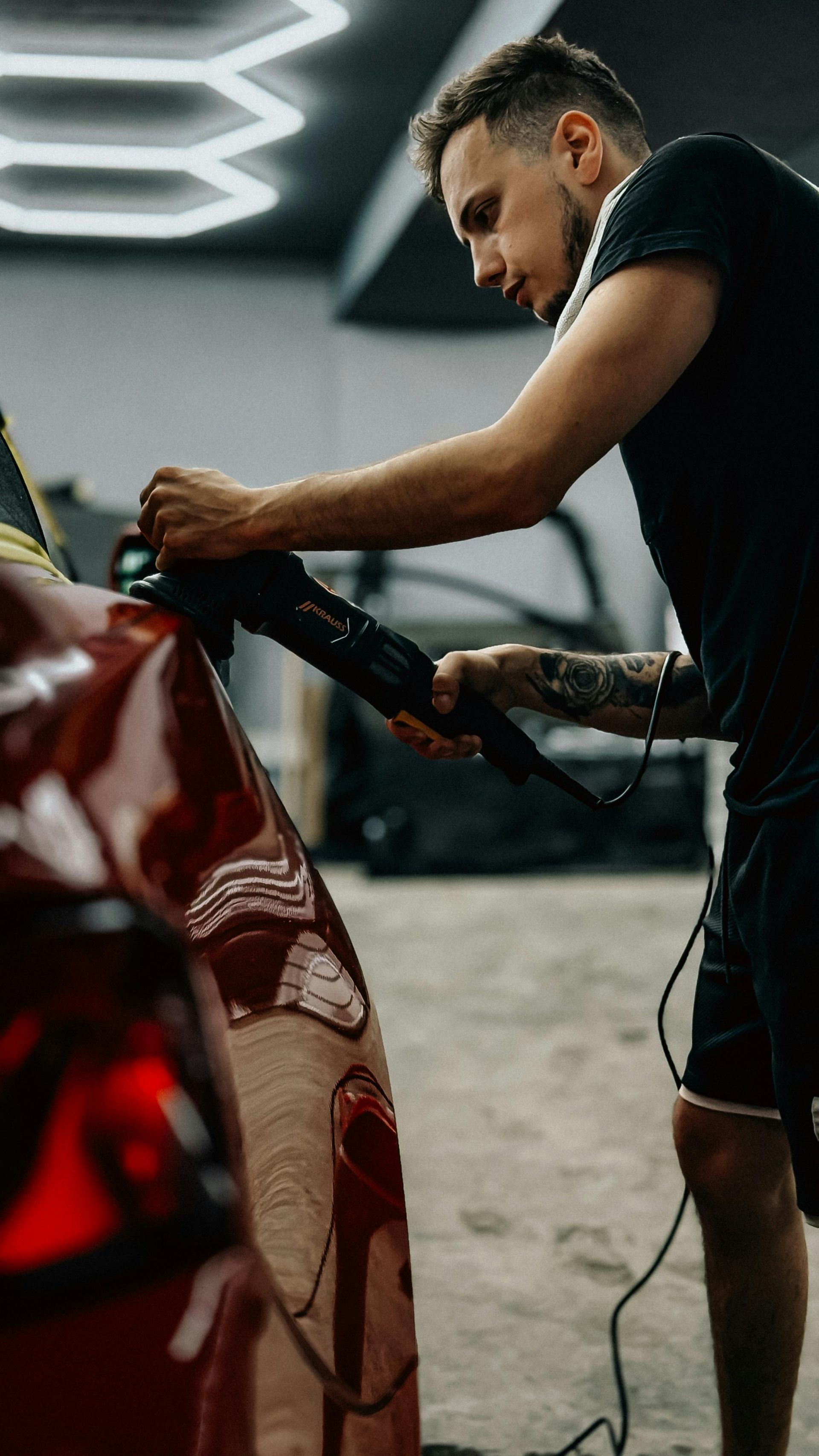 Man polishing a red car with a power tool in a workshop