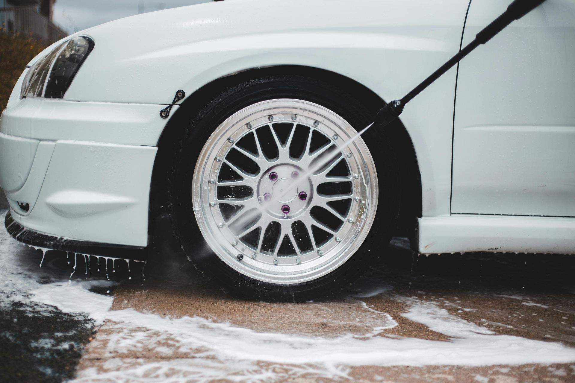 White sports car front wheel close-up in a snowy driveway, with water spraying from the tire.