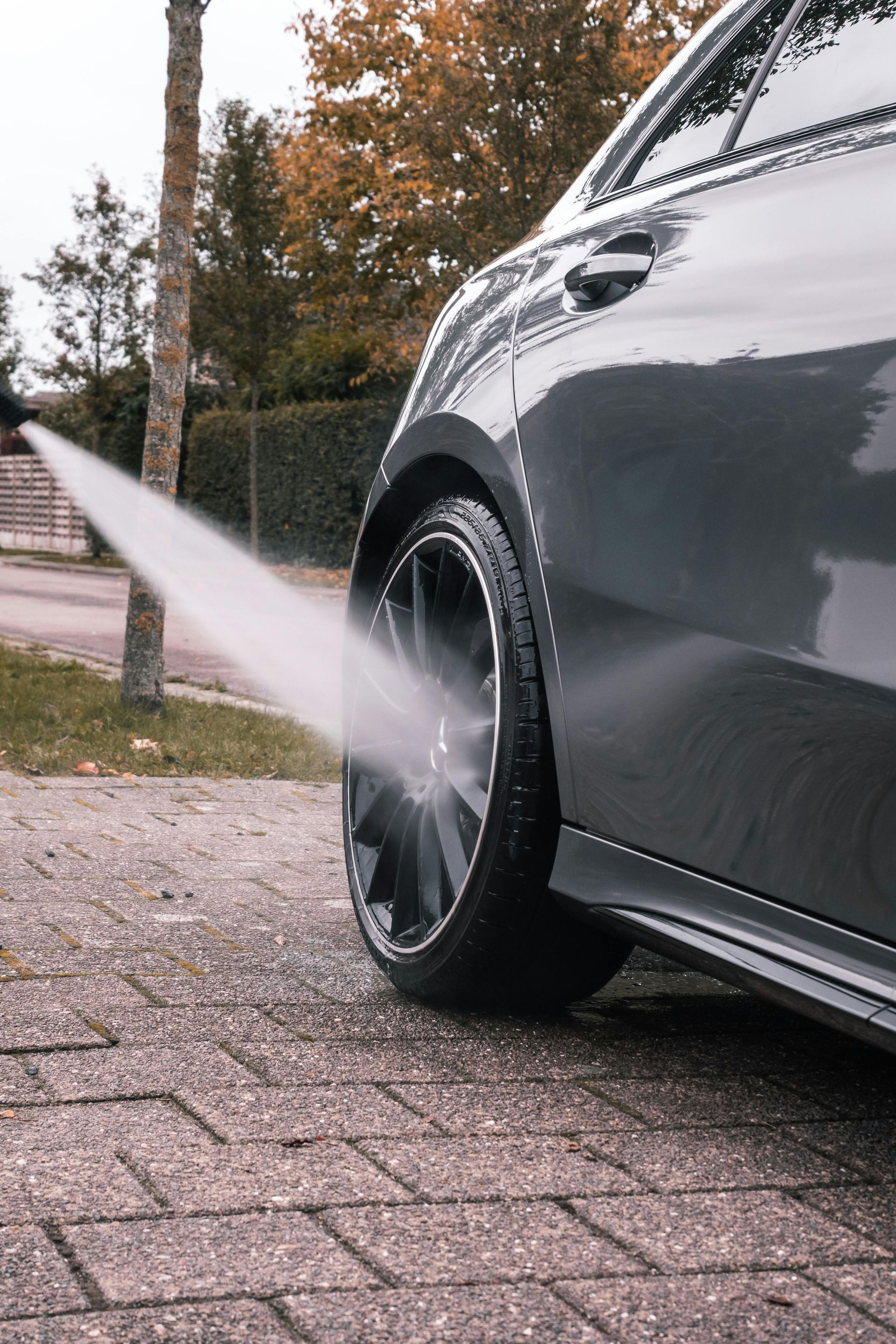Car spraying water from its rear wheel on a wet brick driveway outdoors