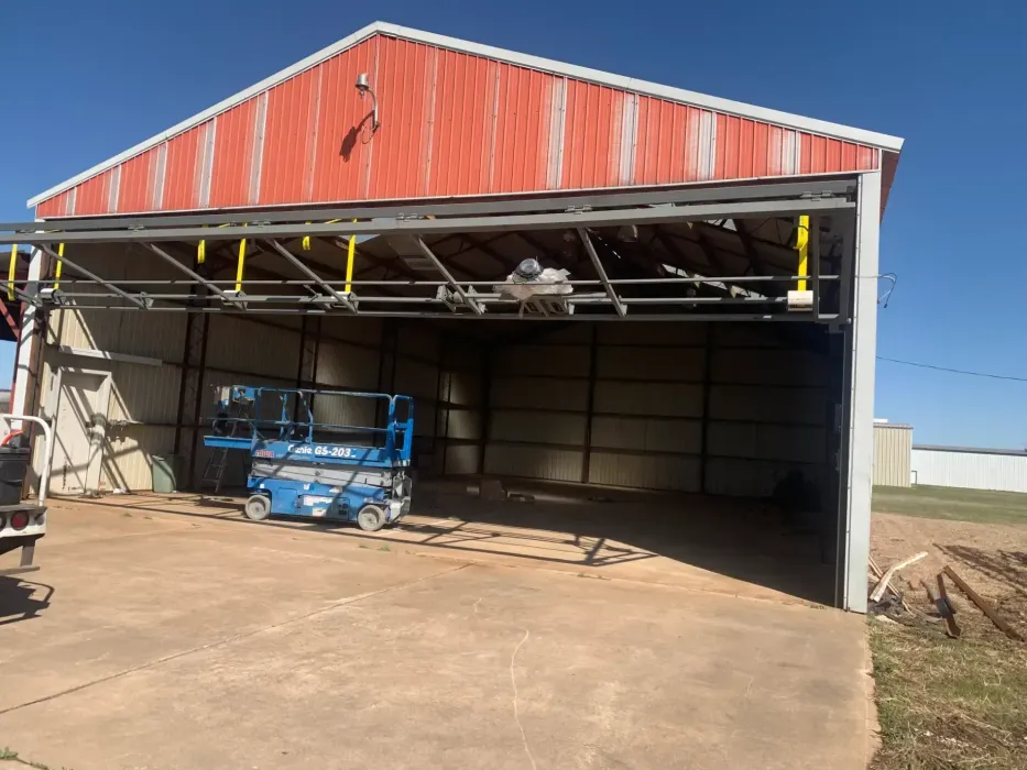 Red barn with open door, a blue lift is inside, and a concrete driveway.