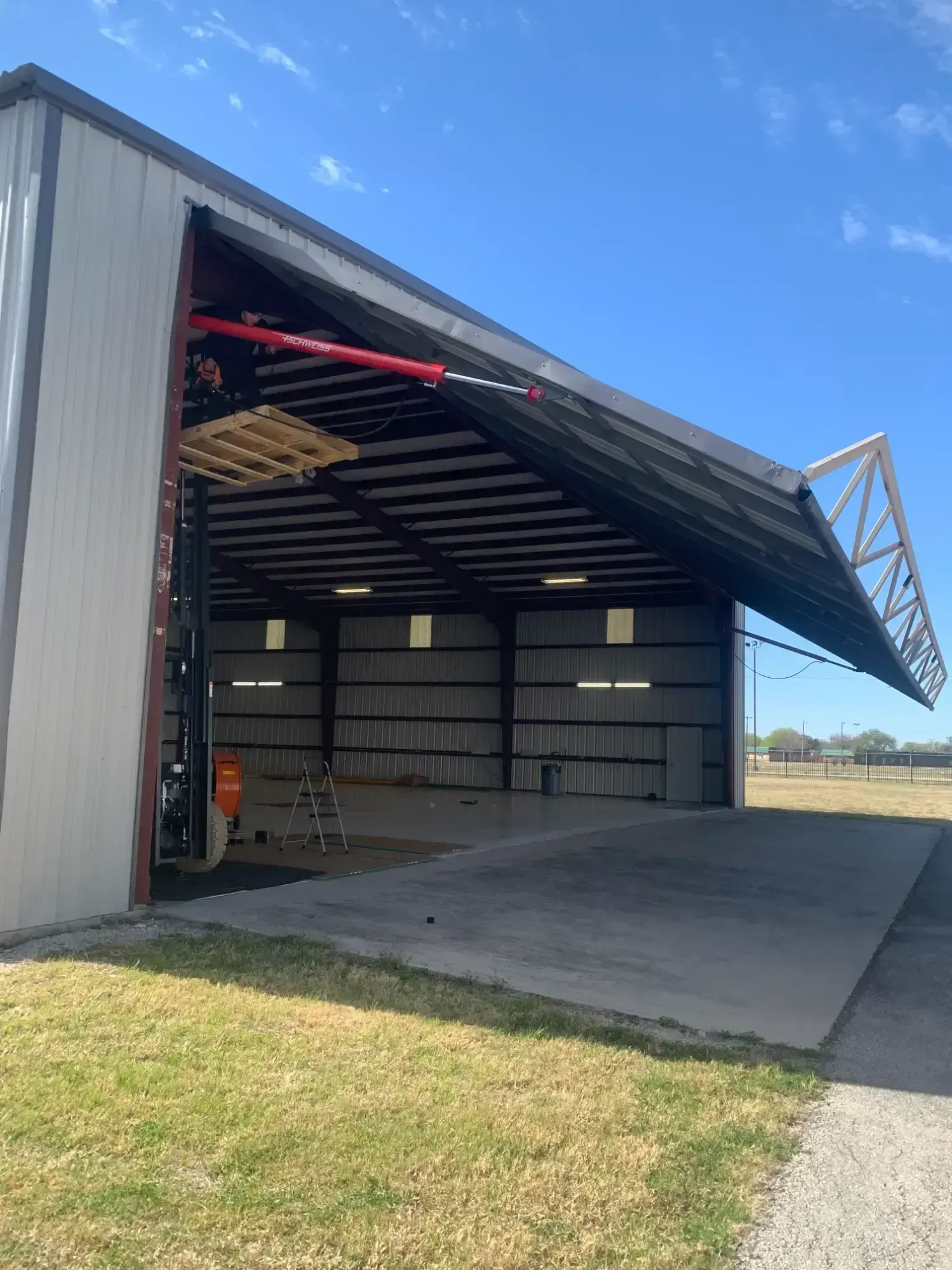 A metal hangar with an open door. The roof is raised, concrete ramp at the entrance.