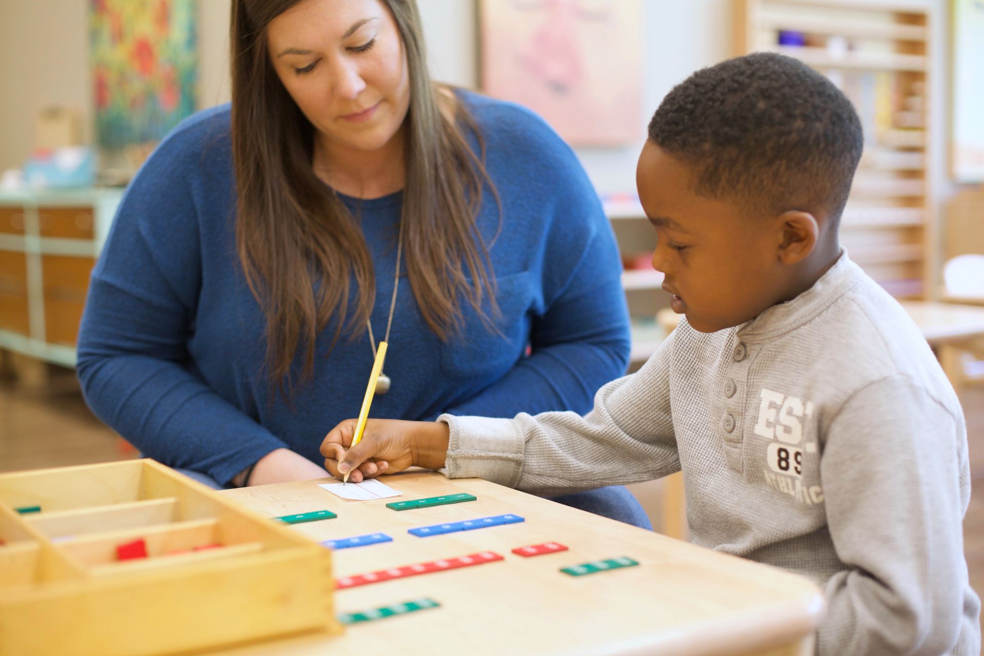 Teacher helping child with the stamp game at a classroom table