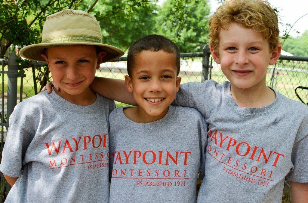 Three elementary-aged boys are wearing grey tshirts with Waypoint Montessori on the front.