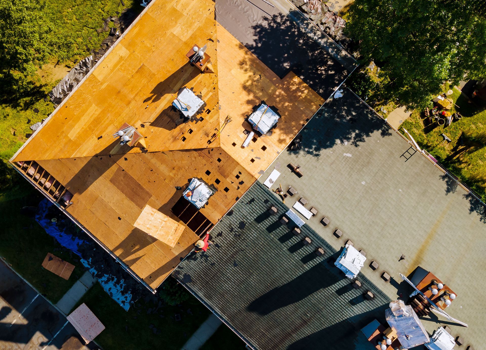 Overhead view of a building roof under renovation; sections of new and old shingles are visible.