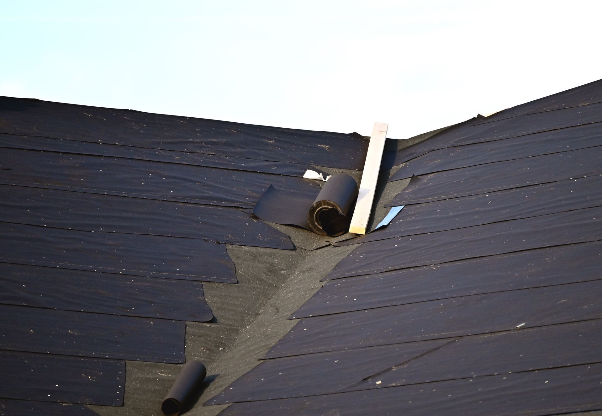 Damaged asphalt shingle roof, torn at a valley with rolled-up material.