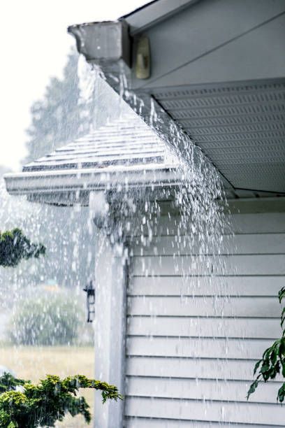 Rain pouring from a white gutter on a house, overcast day.
