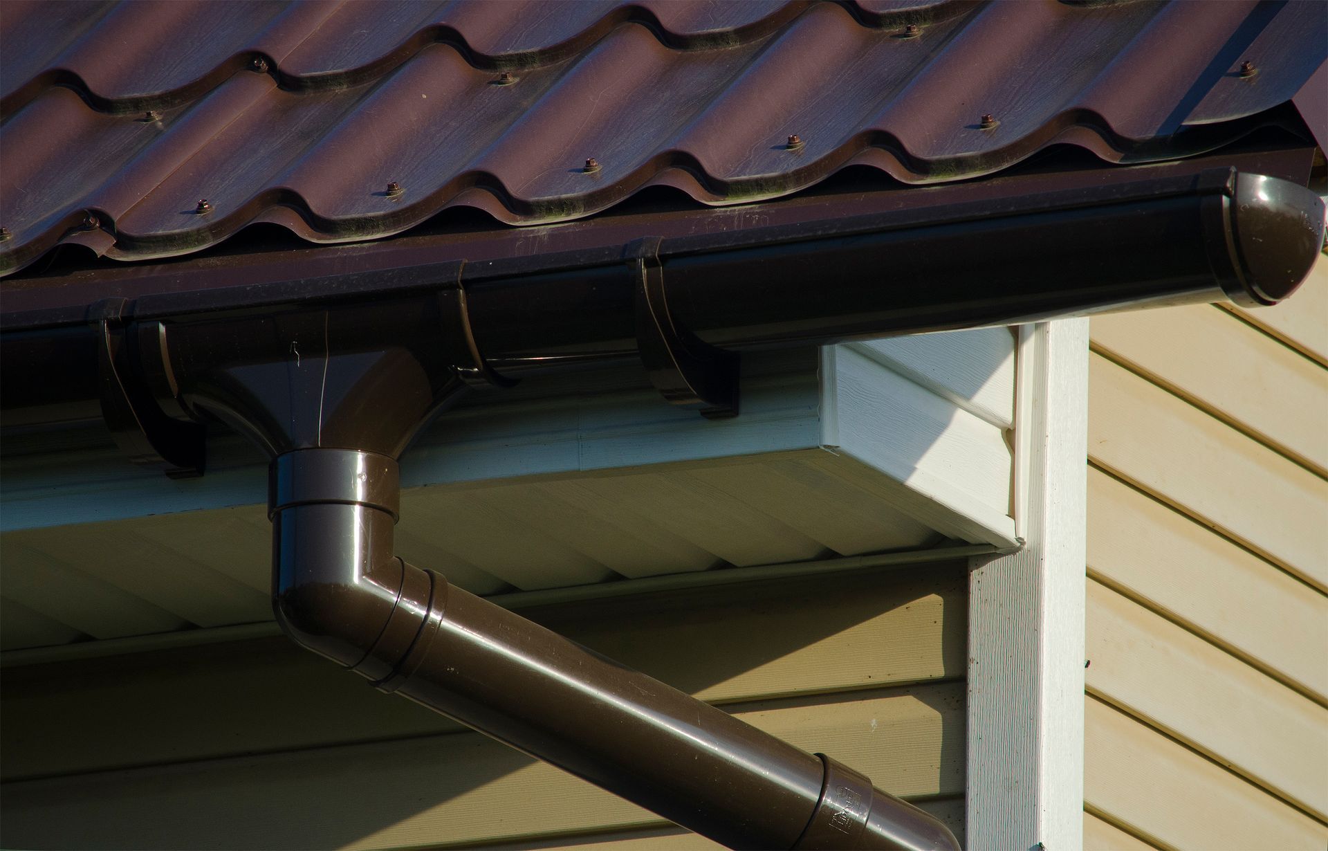 Brown rain gutter system on a building with a brown roof and tan siding.