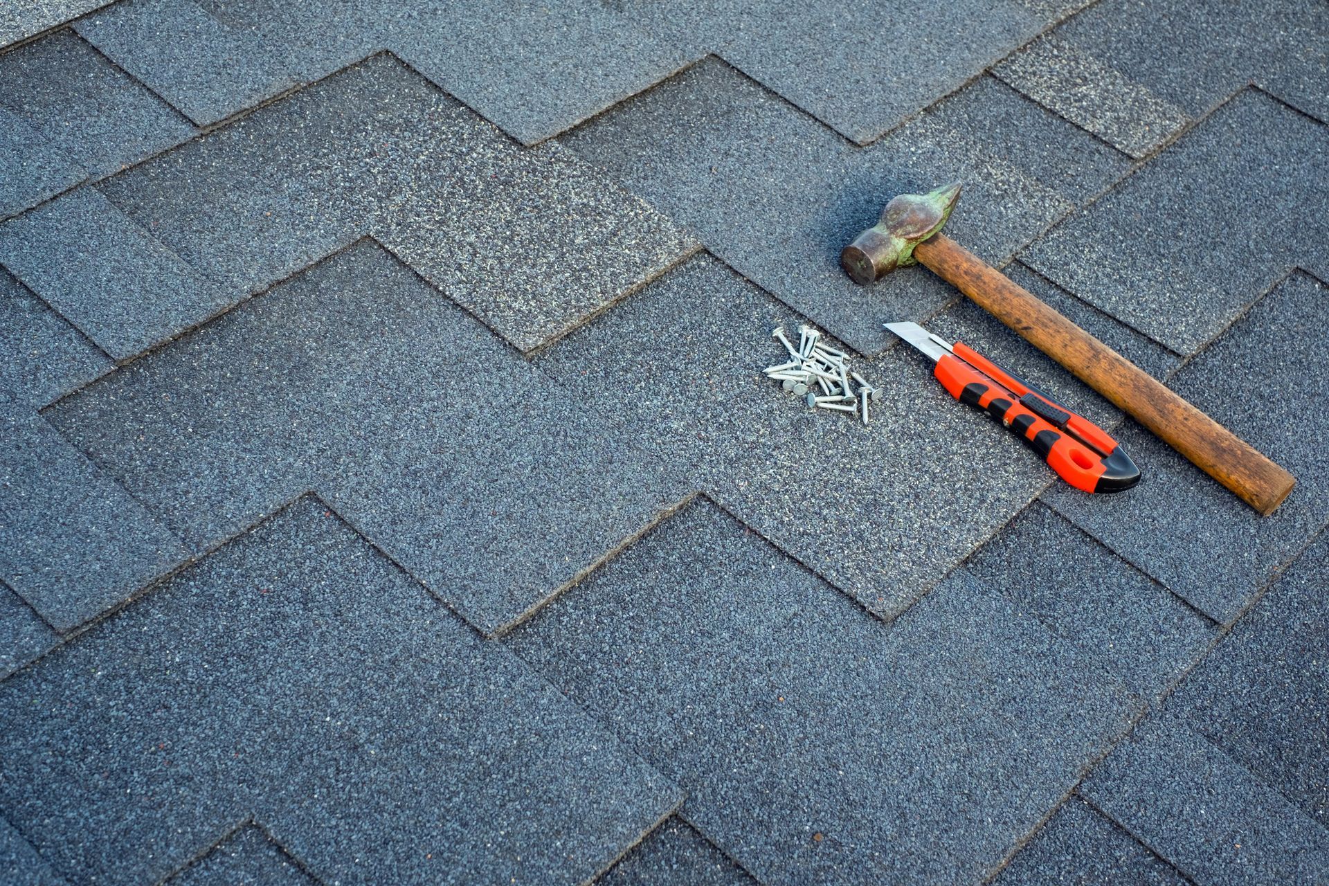 Roof shingles, hammer, utility knife, and nails on a roof.