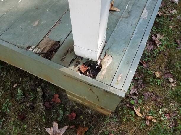 Damaged wooden deck corner with a white support post; green painted boards are rotting and missing pieces.