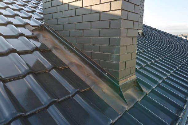 Dark green tiled roof with a brick chimney and metal flashing.