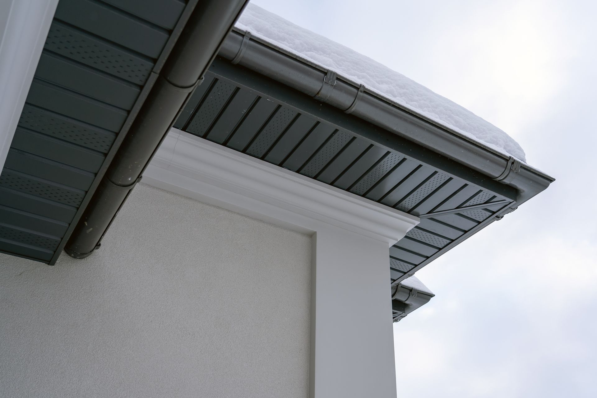 Gray roofline with dark gray siding and a white decorative trim against a cloudy sky.