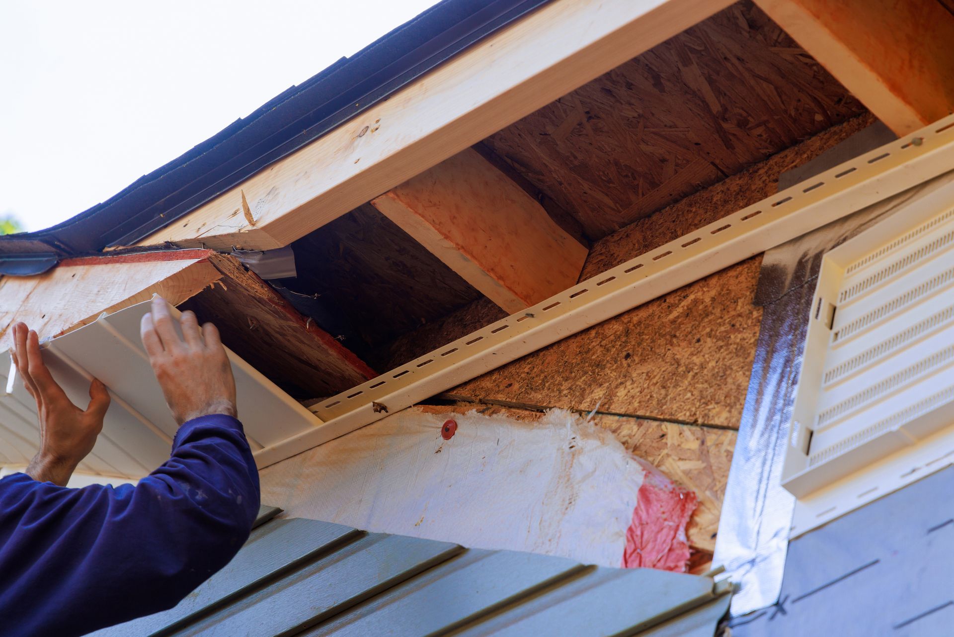Person installing siding on a house. Wooden roof edge exposed.