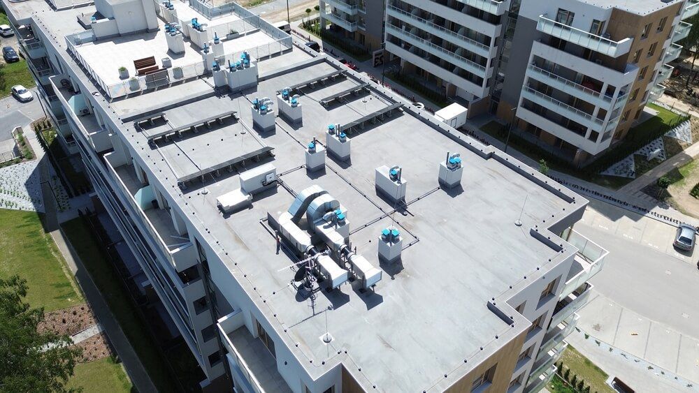 Overhead view of a flat rooftop with various vents, machinery, and air conditioning units on an apartment building.
